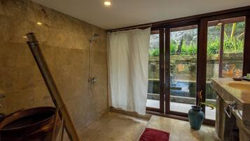 Ein Badezimmer mit Dusche, Waschbecken und Blick auf einen Garten durch eine Glastür.