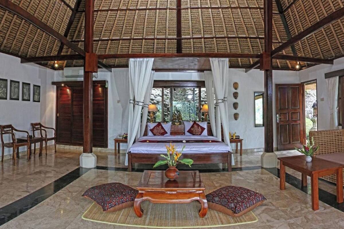A spacious room with a large bed, a sitting area with a table and chairs, and a view through a window.
