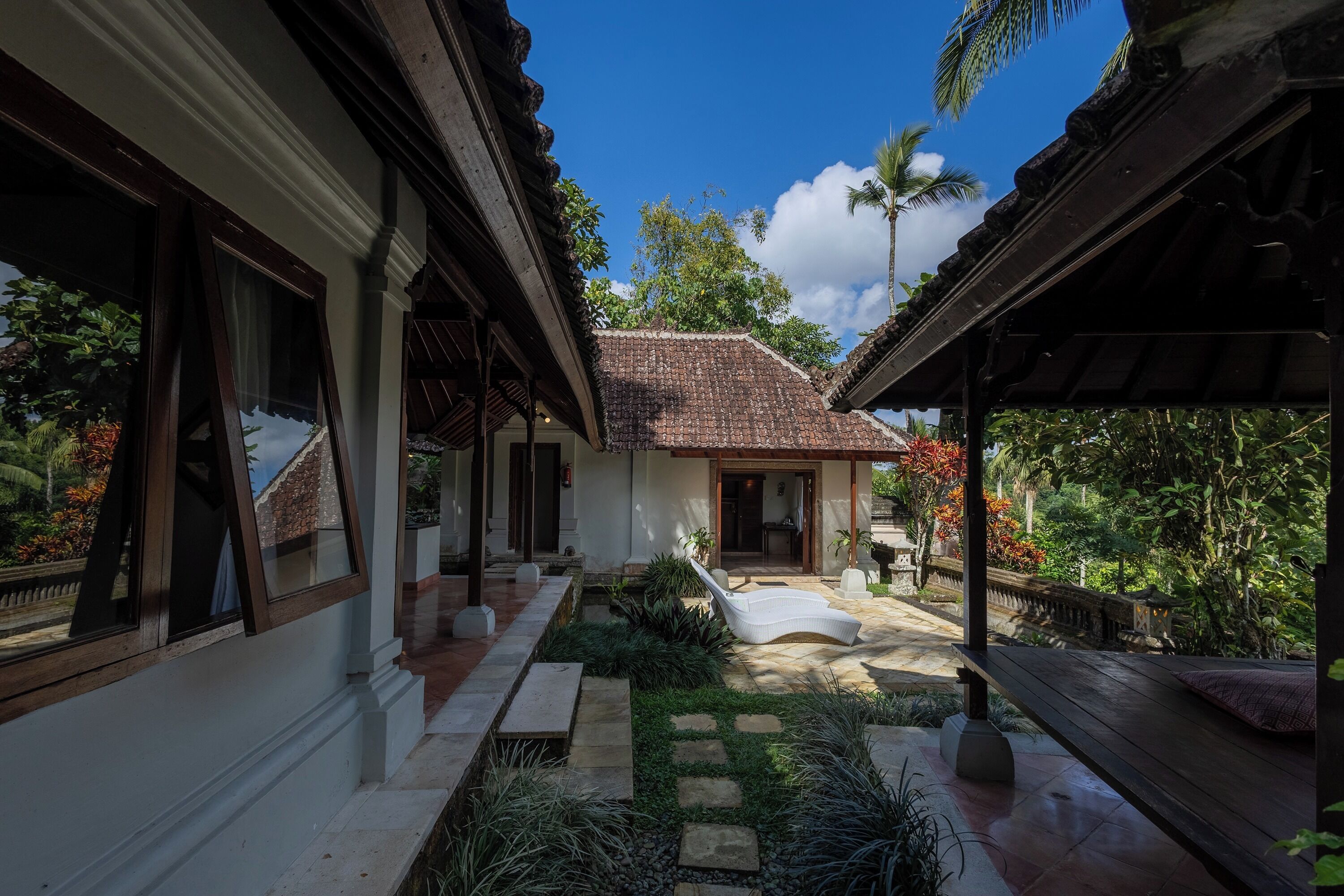 A traditional house with a tiled roof, a covered walkway, and a garden area with a bench.