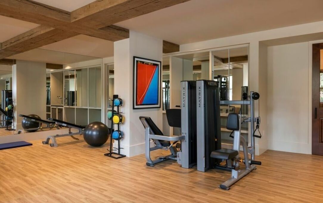 A gym with exercise equipment, a mirrored wall, and a wooden floor.