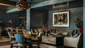 Ein modernes Wohnzimmer mit einer dunkelblauen Wand, einem Holzregal, einem runden Spiegel, einem Esstisch mit Stühlen, einer Couch und einem Couchtisch.