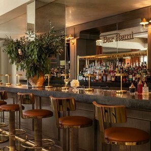 Eine Bar mit Theke, Hockstühlen und einer großen Topfpflanze.