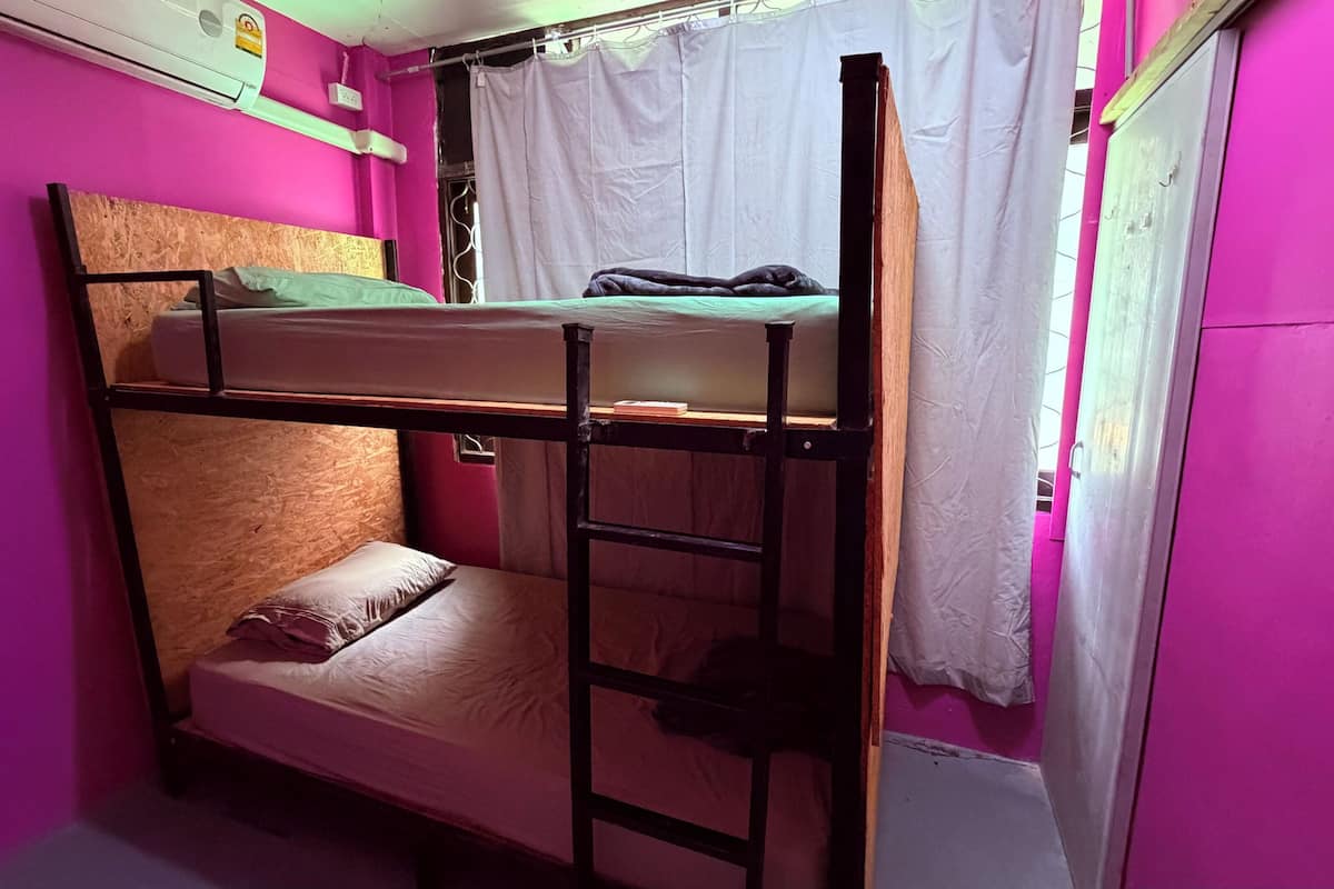 A bunk bed room with a ladder, a window with curtains, and a white air conditioning unit.