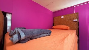 A single bed with an orange bedspread and a gray blanket, a wooden headboard, and a purple wall.
