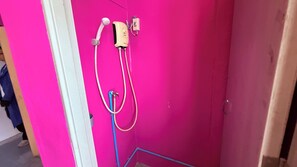 A bathroom with a pink wall, a shower, and a visible electrical outlet.