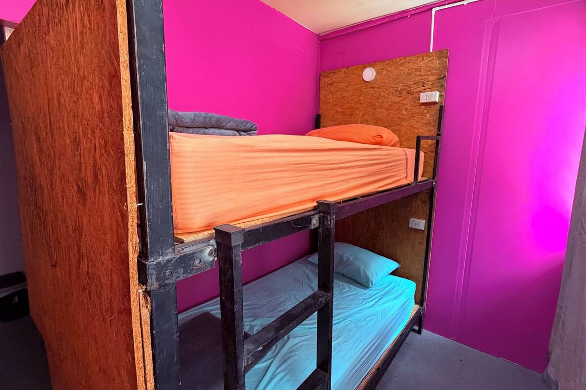 A bunk bed with a wooden headboard, a lower bunk with a blue mattress, and a top bunk with an orange mattress.