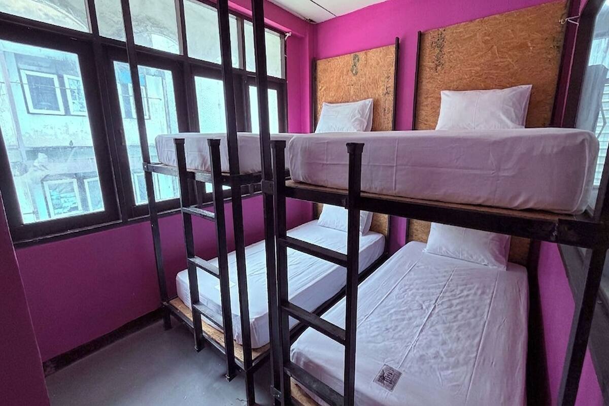 A room with bunk beds, a wooden headboard, and a window with a view of buildings.