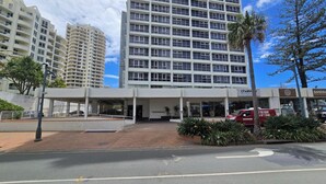 A hotel entrance with a covered walkway, a red van parked outside, and a palm tree. - Beachside Ocean View 1BR Apartment Central Surfers (Surfers Paradise)