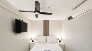 A hotel room with a bed, a ceiling fan, a TV, bedside lamps, and a wall-mounted heater. - Beachside Ocean View 1BR Apartment Central Surfers (Surfers Paradise)