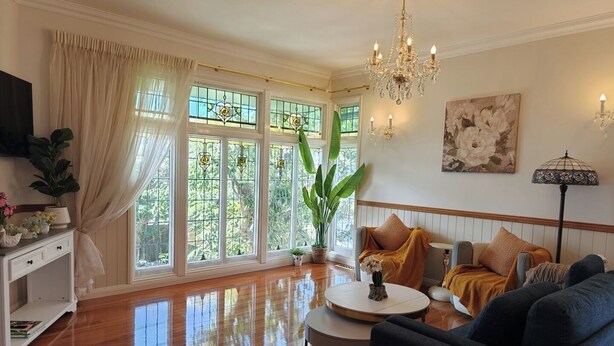 A spacious living room with large windows, a chandelier, a round coffee table, and a sofa with multiple cushions. - 4BR Upper House Close to Blue Mountains Highlights (Katoomba)