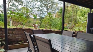 Eine Terrasse im Freien mit Tisch und Stühlen, umgeben von einer Steinmauer und viel Grün.