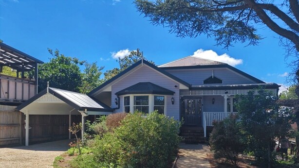 Ein zweigeschossiges Haus mit einer überdachten Veranda, einer Garage und einem gepflegten Garten.