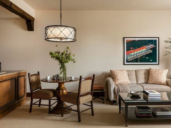 Een gezellige woonkamer met een ronde tafel, twee stoelen, een bank en een salontafel. Aan de muur hangt een schilderij en op de tafel staat een vaas met bloemen.