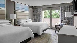 Een hotelkamer met twee bedden, een bank, een televisie en een balkon met uitzicht op groen.
