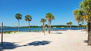 Een strand met palmbomen, ligstoelen en een helderblauwe lucht.