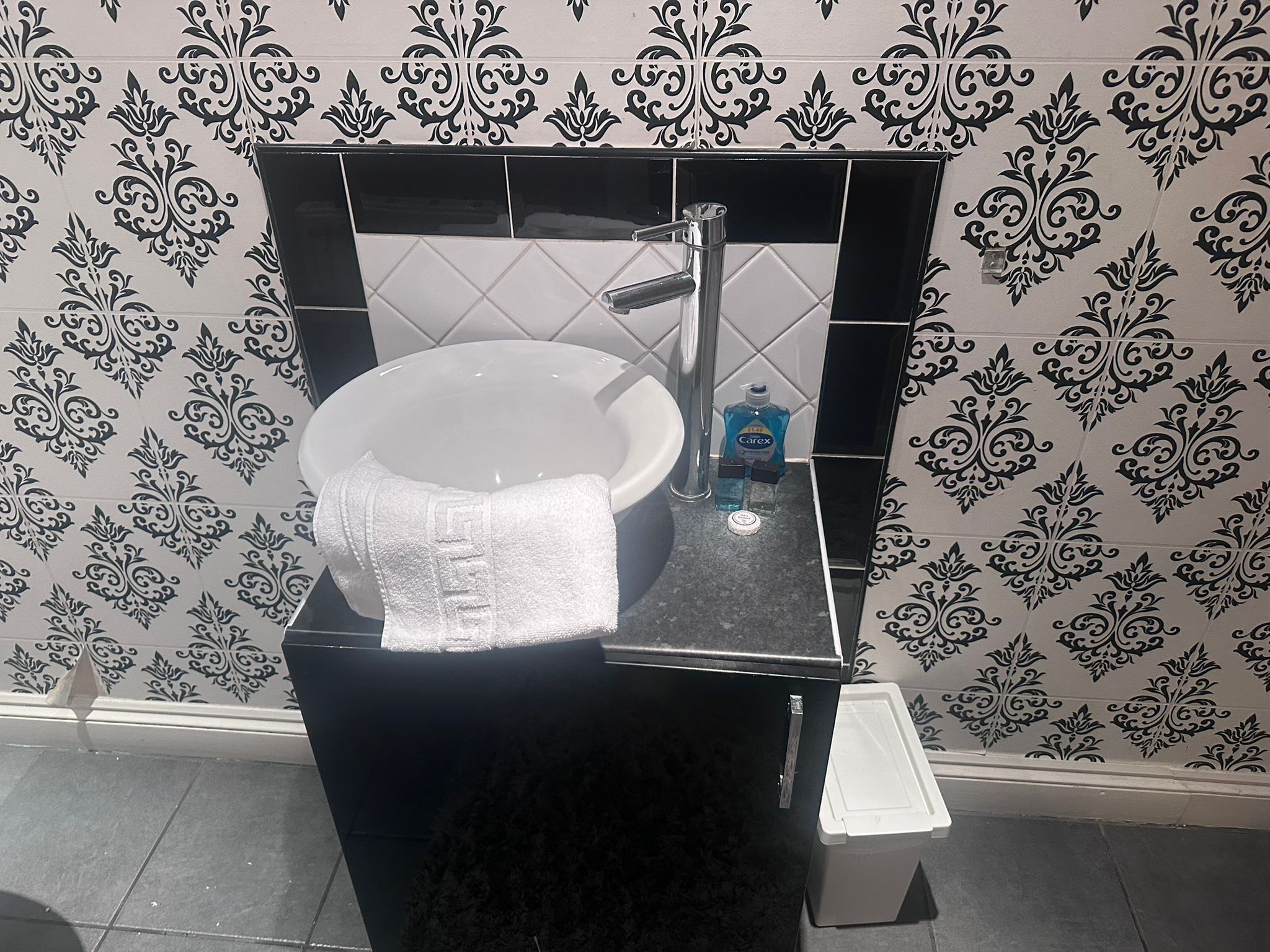 Een badkamer met een zwart wastafel, witte tegels en een decoratief muurpatroon.