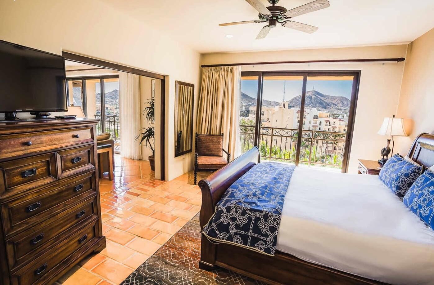 Een hotelkamer met een bed, een dressoir, een televisie en een balkon met uitzicht op gebouwen en bergen.
