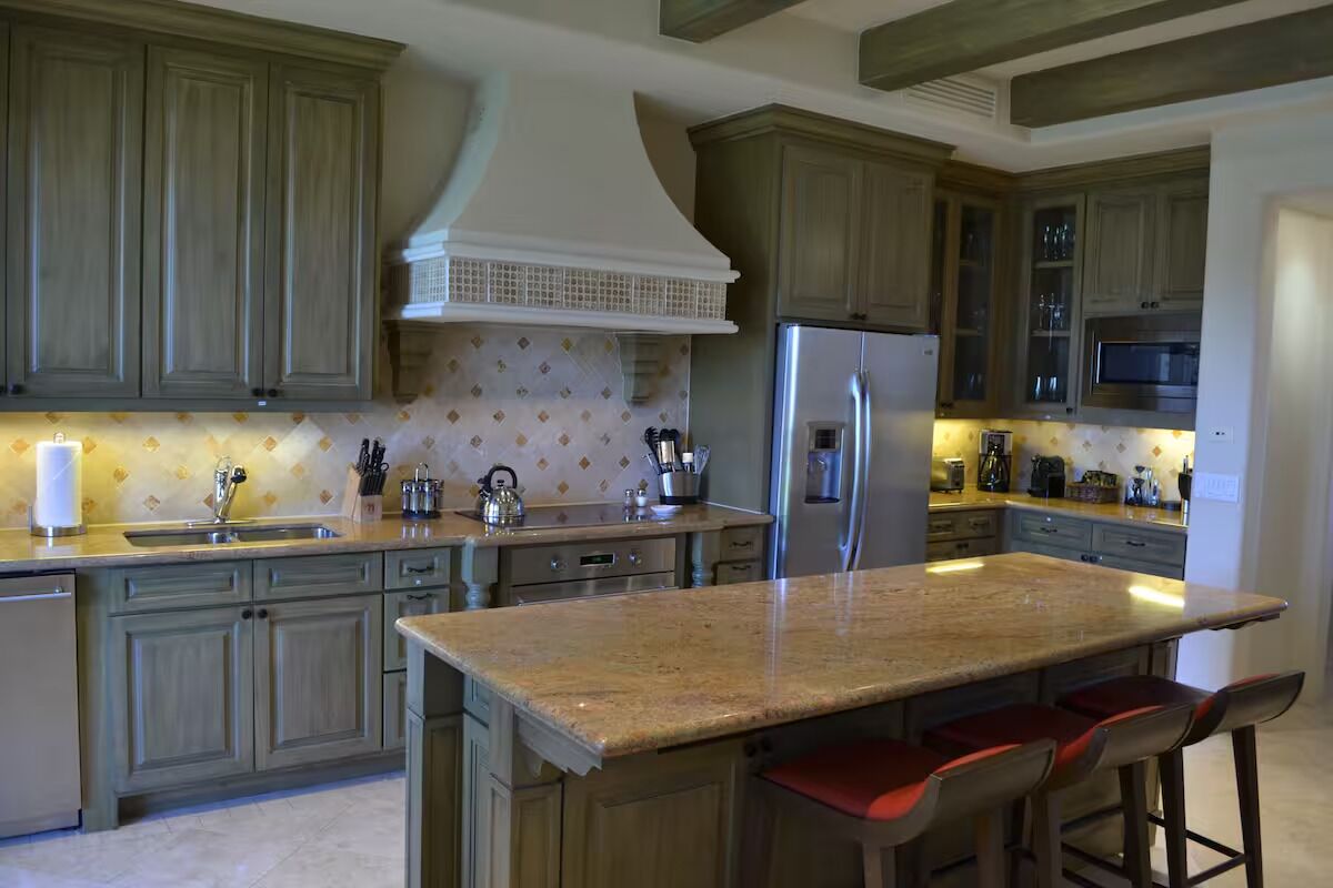 Eine Küche mit Holzausstattung, einem Edelstahlkühlschrank, einer Granitarbeitsplatte und Barhocker.