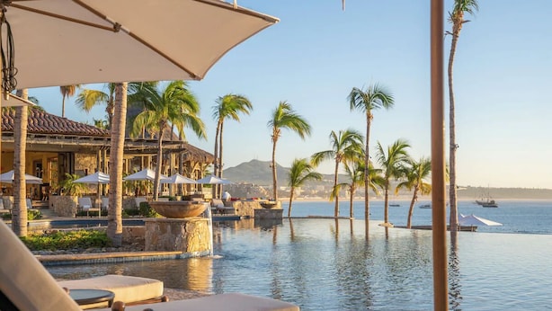 An infinity pool with palm trees, lounge chairs, and umbrellas, overlooking a body of water with boats. - Hacienda Beach Club | 3BR Plus | Den Retreat, Marina | 2 Units (Cabo San Lucas)