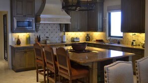 Une cuisine avec des meubles en bois foncé, un îlot central doté de chaises, un four à micro-ondes, un grille-pain et un luminaire suspendu.