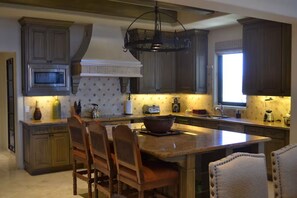 Une cuisine avec des meubles en bois foncé, un îlot central doté de chaises, un four à micro-ondes, un grille-pain et un luminaire suspendu.