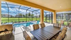 Un portico coperto con piscina, mobili da esterno e barbecue.
