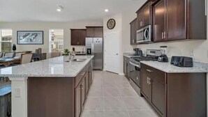 Una cucina moderna con mobili in legno scuro, una grande isola, elettrodomestici in acciaio inossidabile e un pavimento piastrellato.
