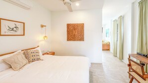 A hotel room with a large bed, a ceiling fan, a wall-mounted air conditioner, a bedside table with a lamp, and a view of the adjacent room through a window with curtains. - Stunning Sea View Bungalow (Tambon Ko Pha-ngan)