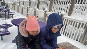 Dos personas sentadas junto a una fogata en un espacio exterior nevado, con mesas y sillas.