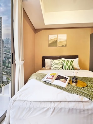 A hotel room with a large bed, a view of the city, and a window with curtains. - Eldoria By SanLiving - Studio (Jakarta)