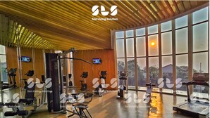Ein großzügiger Fitnessraum mit unterschiedlichen Trainingsgeräten, großen Fenstern und einer Holzbalkendecke.