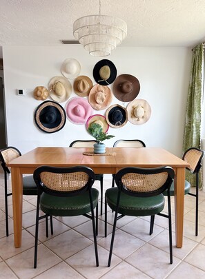 A dining area with a wooden table, black and green upholstered chairs, and a wall decorated with various hats. - Poolside Palms & Oak; heated saltwater pool, 10 min to beach, A/C, dog-friendly (Venice)