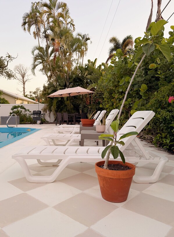 A poolside area with lounge chairs and a small table with a potted plant. - Poolside Palms & Oak; heated saltwater pool, 10 min to beach, A/C, dog-friendly (Venice)