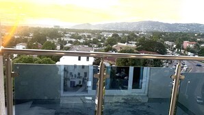 Ein Balkon mit Glasgeländer mit Blick auf eine Stadtlandschaft, Gebäude und eine Bergkette in der Ferne.