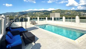 Ein Poolbereich auf dem Dach mit Liegestühlen und Blick auf die umliegende Landschaft.
