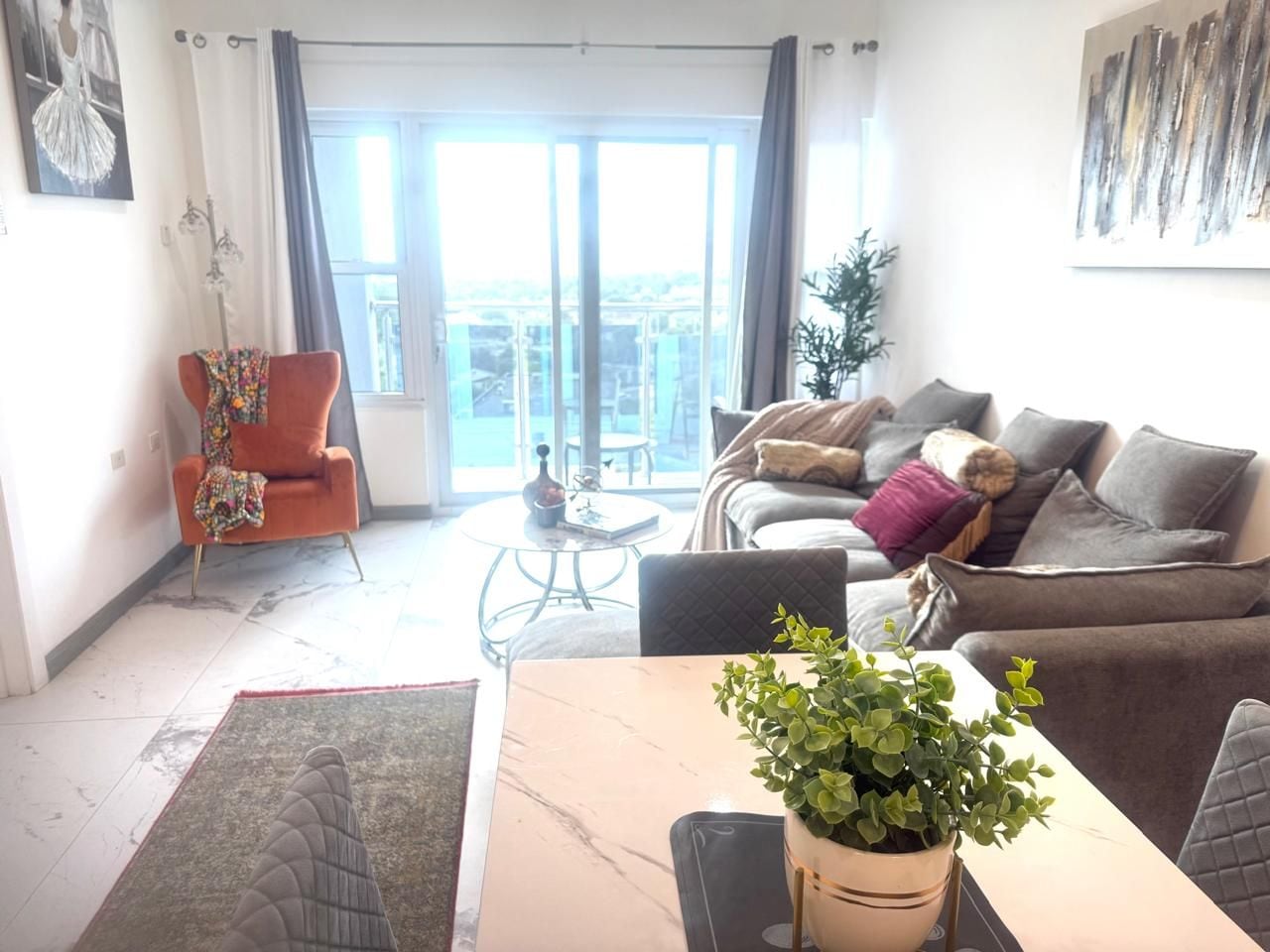 Ein Wohnzimmer mit einer Couch, Sesseln, einem Esstisch mit einer Pflanze und Blick durch eine Glastür.