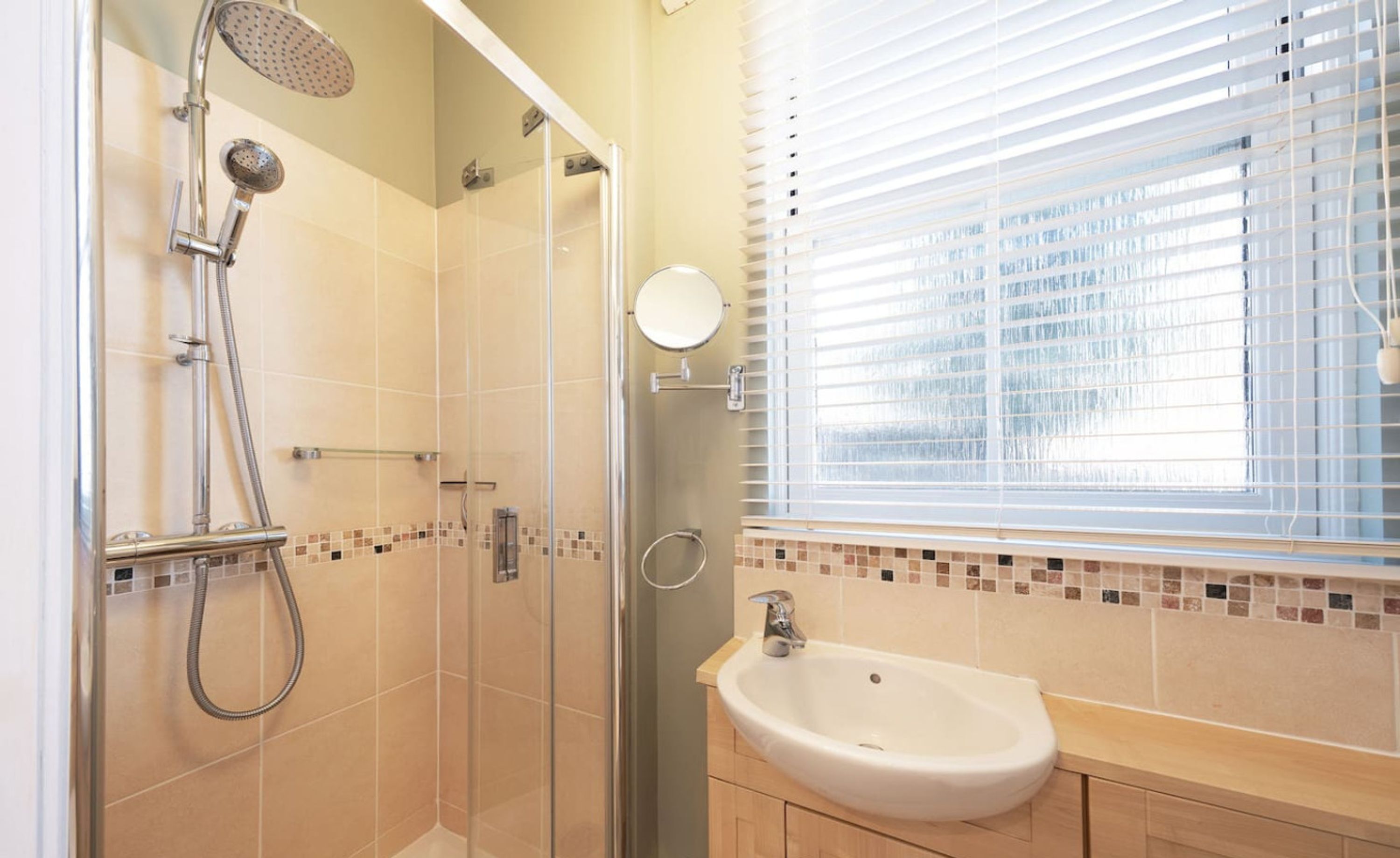 A modern bathroom with a glass-enclosed shower, a sink, and a window with blinds.