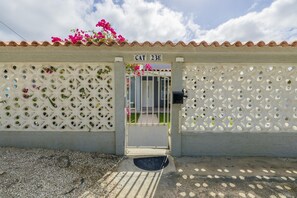 Una entrada protegida con reja metálica, un muro blanco con celosía decorativa y un letrero sobre la reja.