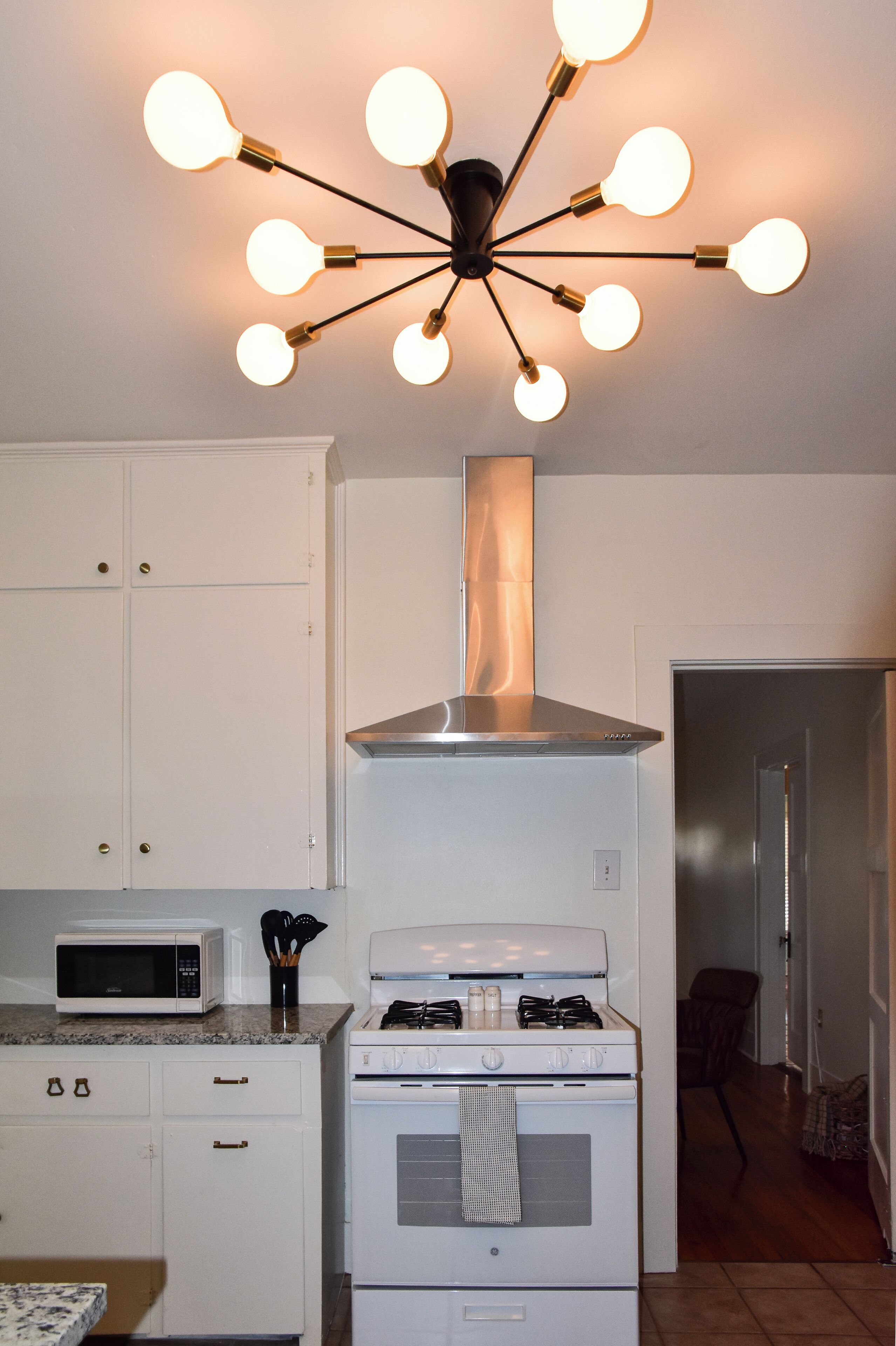 Une cuisine avec des armoires blanches, un four à micro-ondes, une cuisinière et un luminaire moderne.