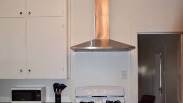Une cuisine avec des armoires blanches, un four à micro-ondes, une cuisinière et un luminaire moderne.