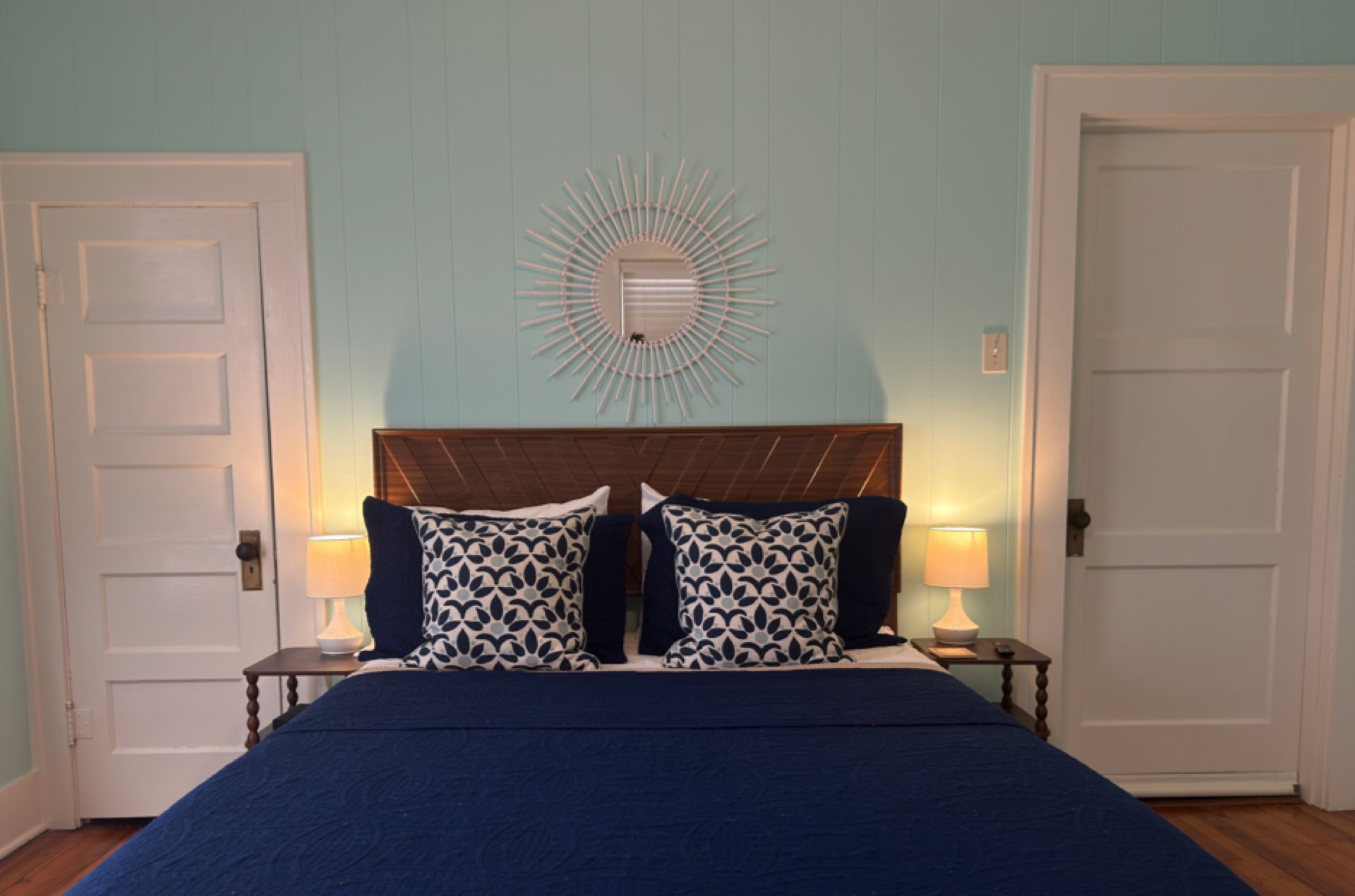 Une chambre à coucher comprenant un lit, deux tables de chevet, un luminaire fixé au mur et deux portes.