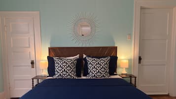 Une chambre à coucher comprenant un lit, deux tables de chevet, un luminaire fixé au mur et deux portes.