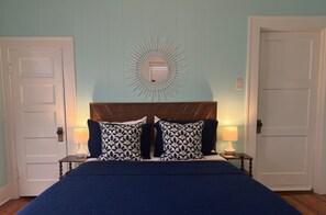 A bedroom with a bed, two nightstands, a wall-mounted light fixture, and two doors.