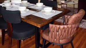 Zona pranzo con tavolo in legno apparecchiato per quattro persone, circondato da sedie, un lampadario e un camino.