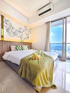 A modern bedroom with a large bed, a decorative wall piece, and a city view through the window. - iOne By SanLiving - Studio (Jakarta)