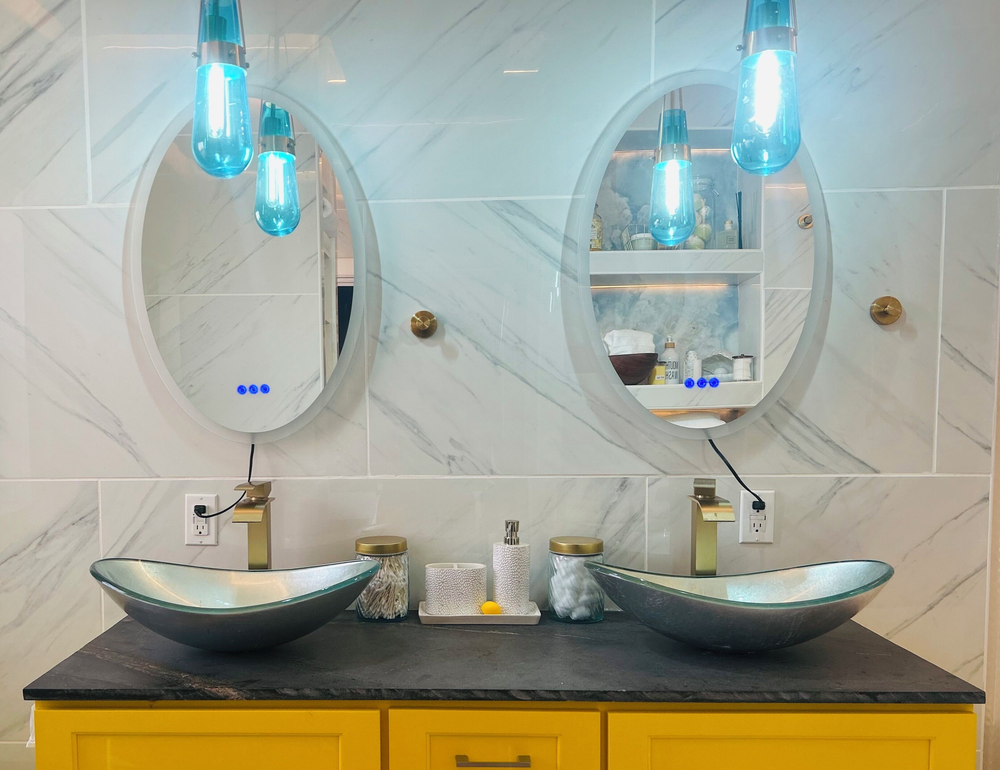 A bathroom with two oval mirrors, a black countertop, and a yellow cabinet.
