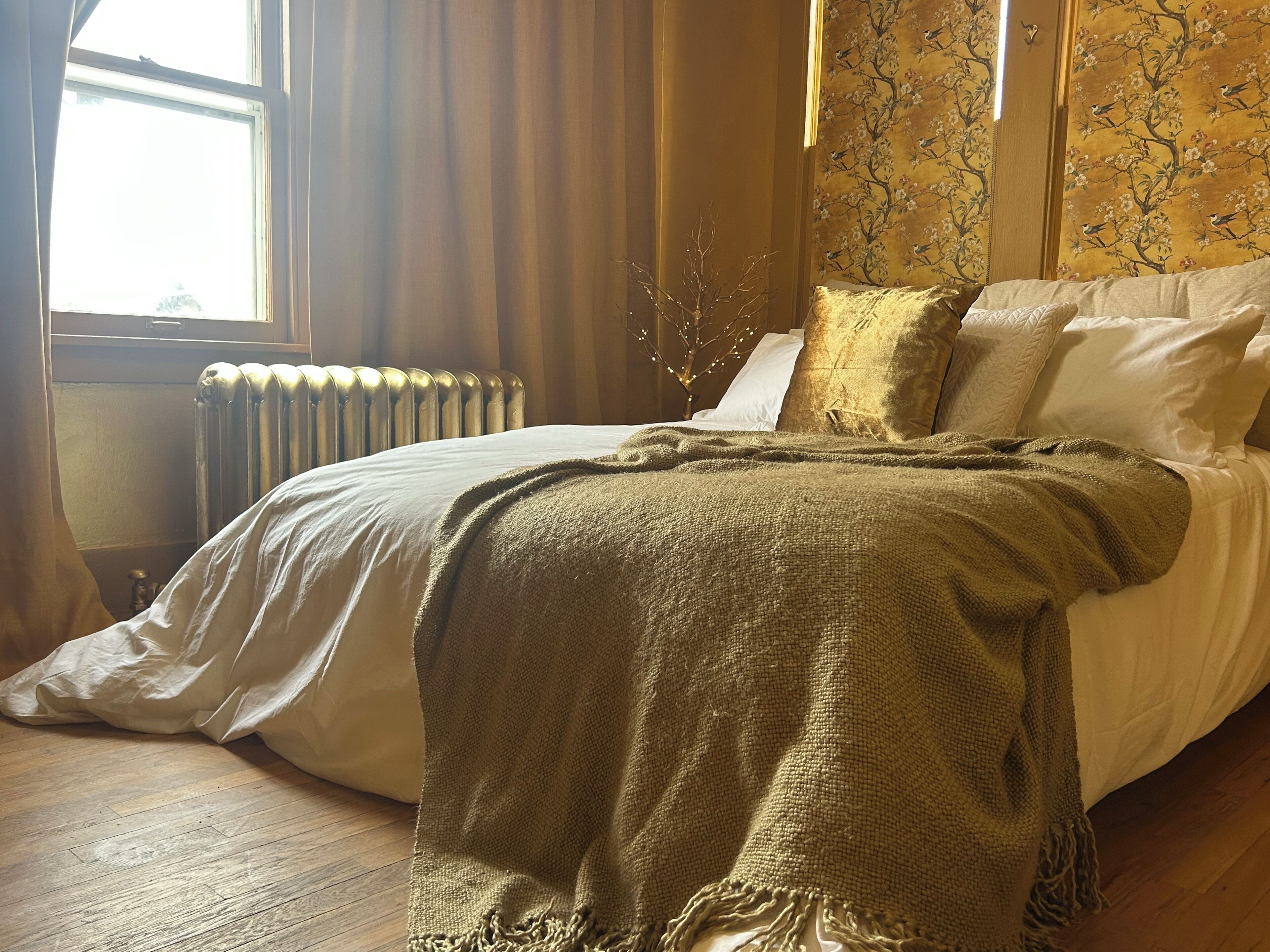 A bedroom with a bed, a radiator, curtains, and a wall with a floral pattern.