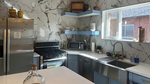Ett modernt kök med marmorbeklädd vägg bakom arbetsbänken, rostfria vitvaror och blå köksluckor.