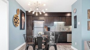 A modern kitchen with dark cabinetry, a stainless steel refrigerator, and a dining area with a glass table and metal chairs. - Updated 2 Bed 2 Bath Condo on beautiful Lake Hamilton 7 minutes from Oaklawn!! (Lake Hamilton)