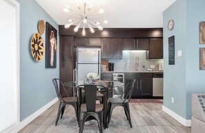 A modern kitchen with dark cabinetry, a stainless steel refrigerator, and a dining area with a glass table and metal chairs. - Updated 2 Bed 2 Bath Condo on beautiful Lake Hamilton 7 minutes from Oaklawn!! (Lake Hamilton)